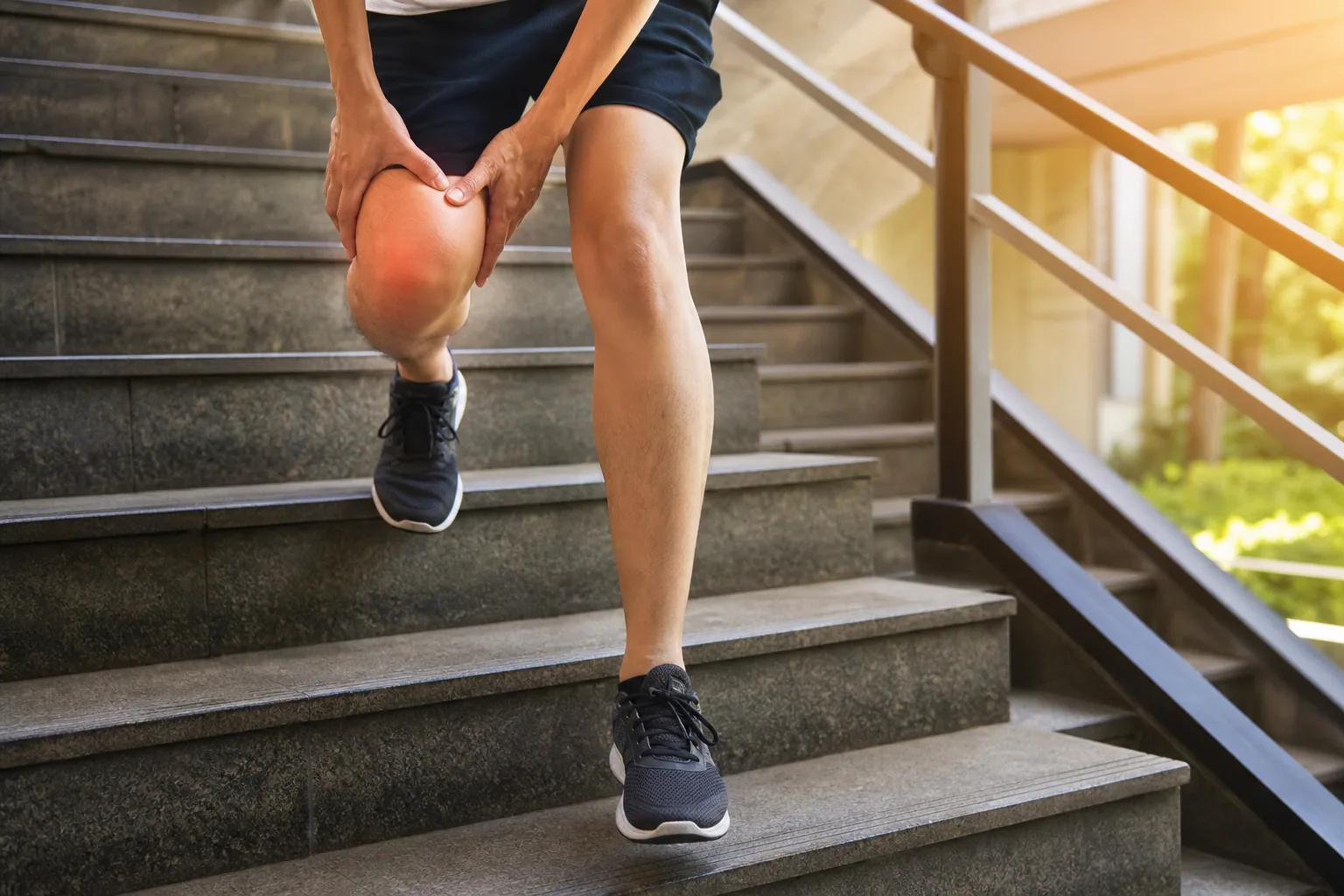 Personne en tenue de sport arrêtée dans un escalier extérieur, main tenant son genou douloureux