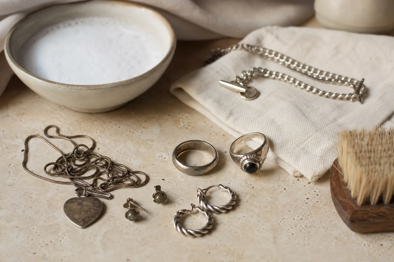 Bijoux en argent, bague et chaîne, posés sur un tissu doux, lumière naturelle chaleureuse